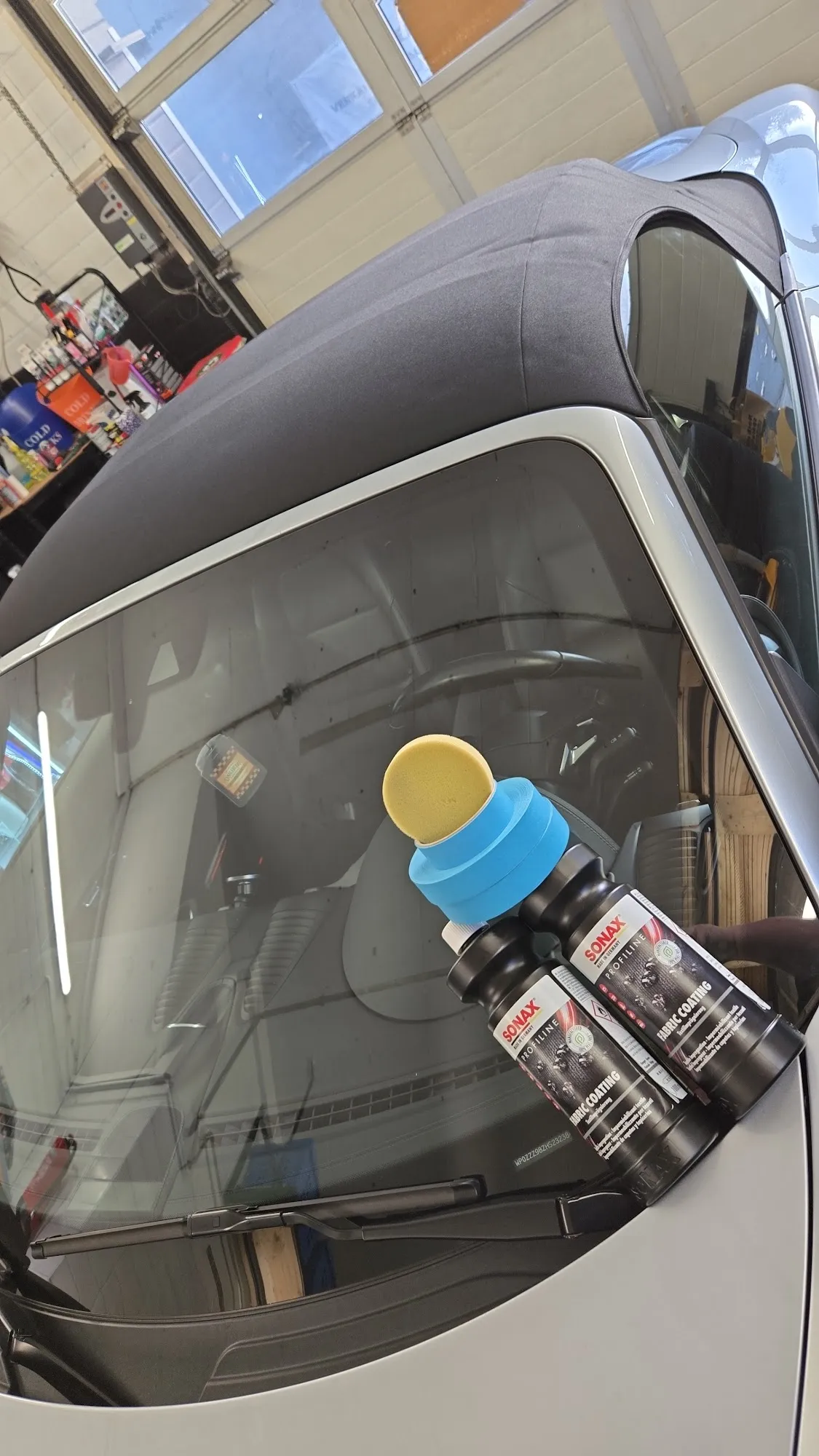 Zwei Flaschen SONAX Fabric Coating auf der Windschutzscheibe eines Cabrios