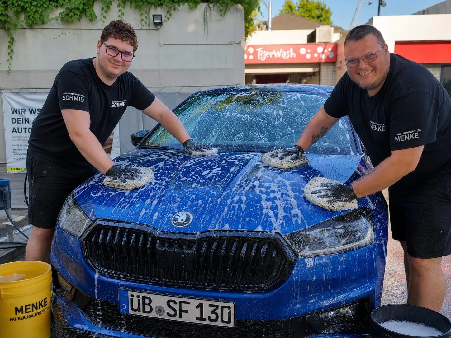 Schmid und Menke in schwarzen Firmen-Shirts beim Einschäumen eines blauen Skoda